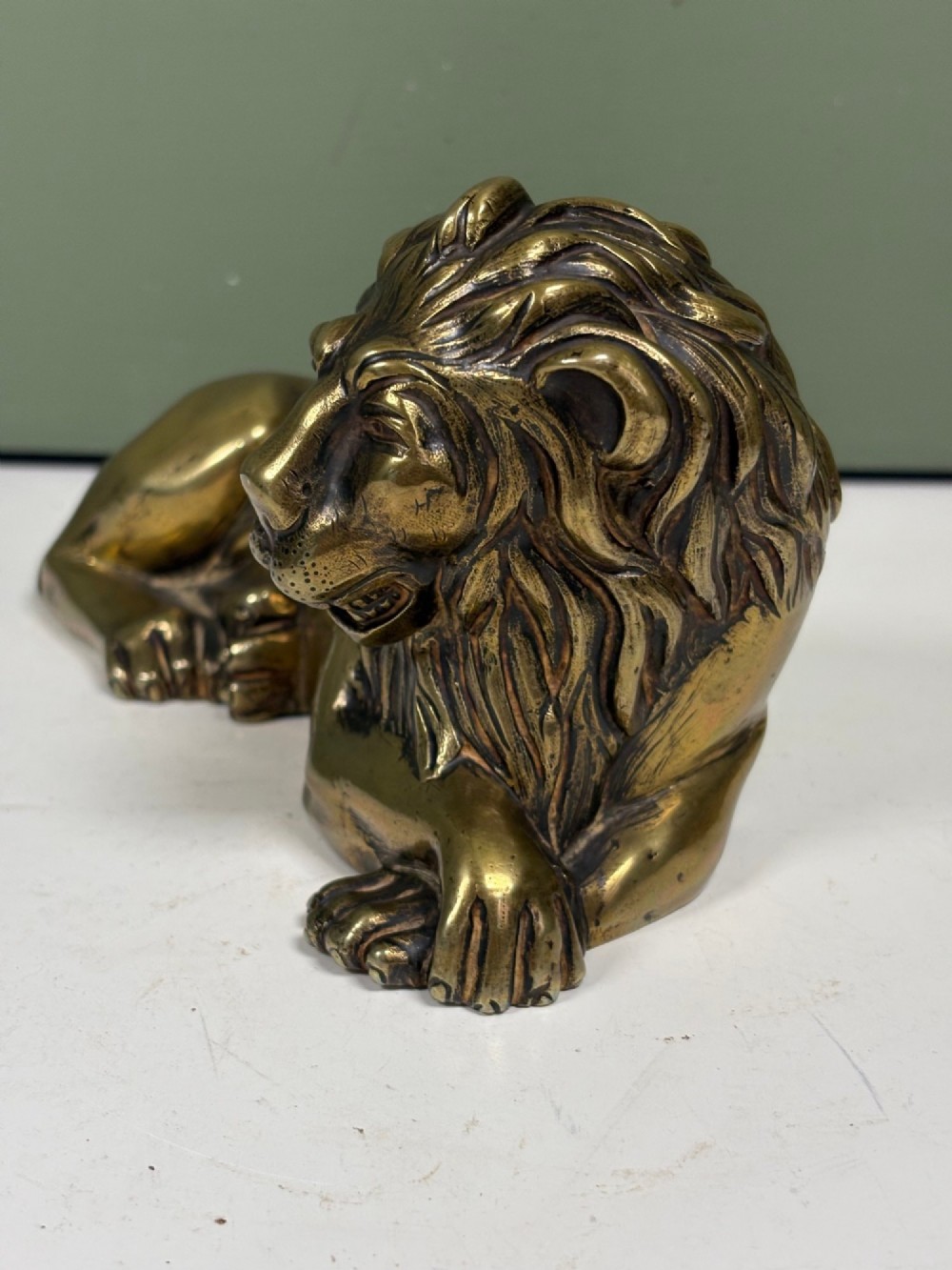 A pair of cast brass figures depicting recumbent lions with detailed manes and crossed paws facing forward. View VI