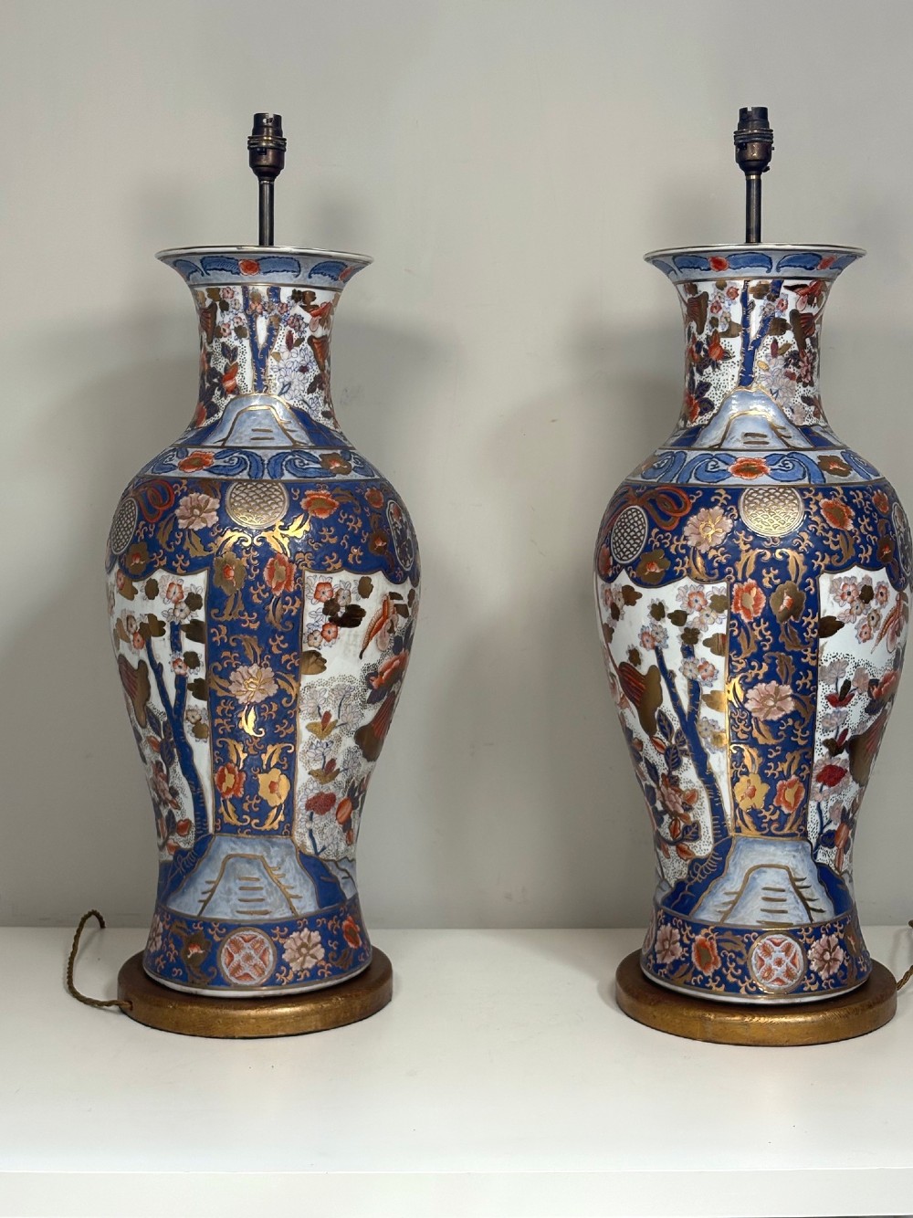 A pair of large ceramic baluster-shaped lamps decorated with traditional Japanese Imari floral patterns in blue, red, and gold, mounted on circular wooden plinths. View II