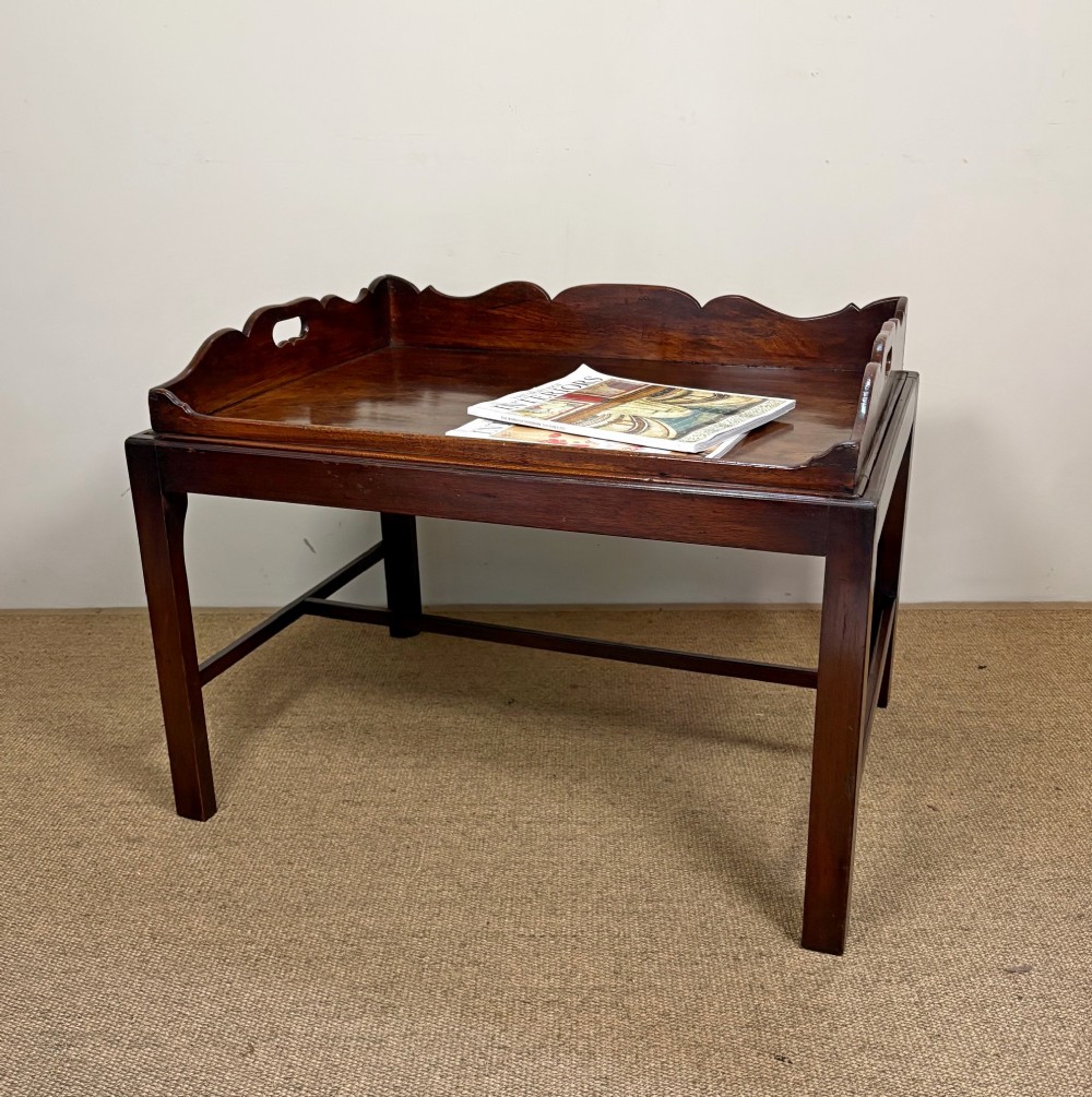 A George III mahogany butlers tray table featuring a scalloped gallery edge with cut-out handles supported by a square-leg wooden stand with cross stretchers. View III