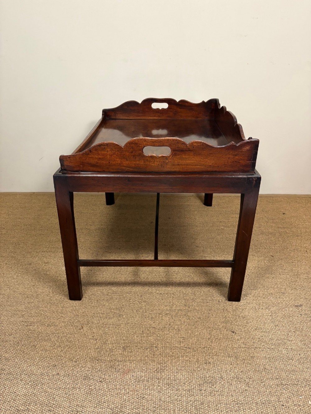 A George III mahogany butlers tray table featuring a scalloped gallery edge with cut-out handles supported by a square-leg wooden stand with cross stretchers. View IV
