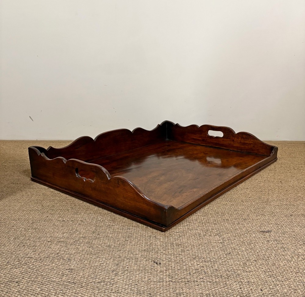 A George III mahogany butlers tray table featuring a scalloped gallery edge with cut-out handles supported by a square-leg wooden stand with cross stretchers. View VI