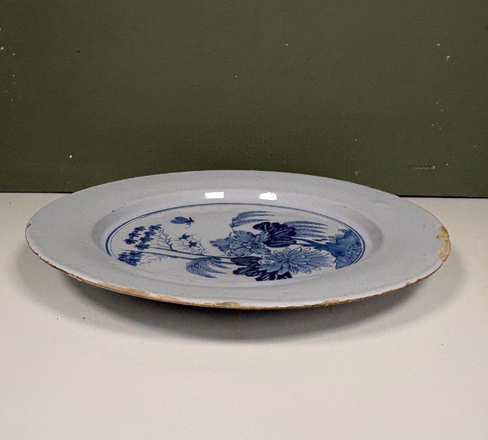 An 18th-century circular blue and white tin-glazed earthenware charger featuring a central hand-painted floral motif with a butterfly detail. View IV