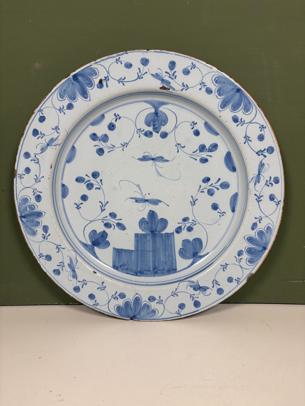 An 18th-century circular blue and white Delftware charger decorated with hand-painted floral and insect motifs.