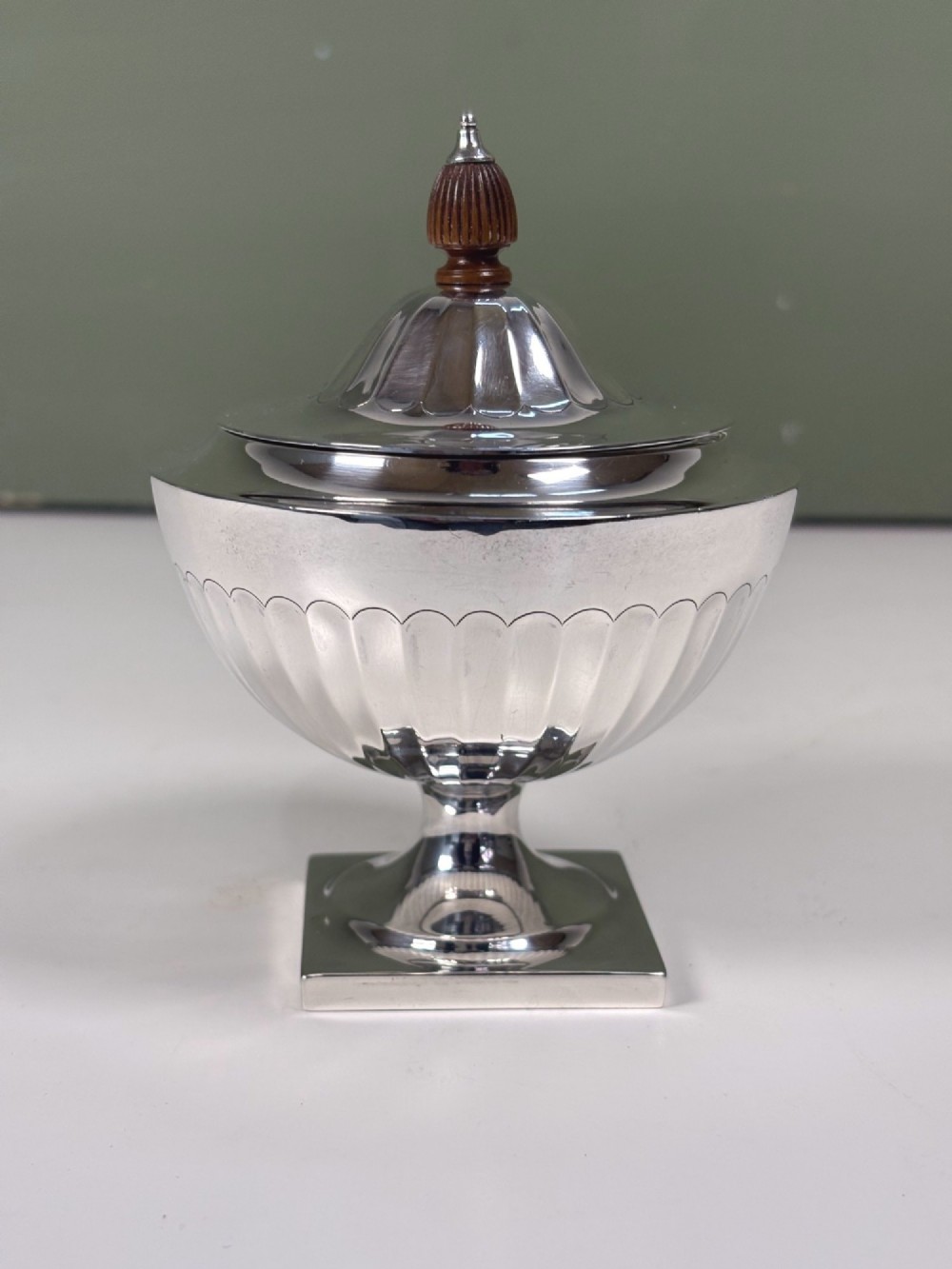 A silver fluted tea caddy with a stepped square base, domed cover, and turned wooden finial.