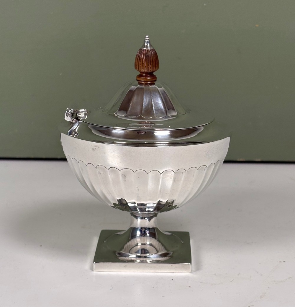 A silver fluted tea caddy with a stepped square base, domed cover, and turned wooden finial. View II