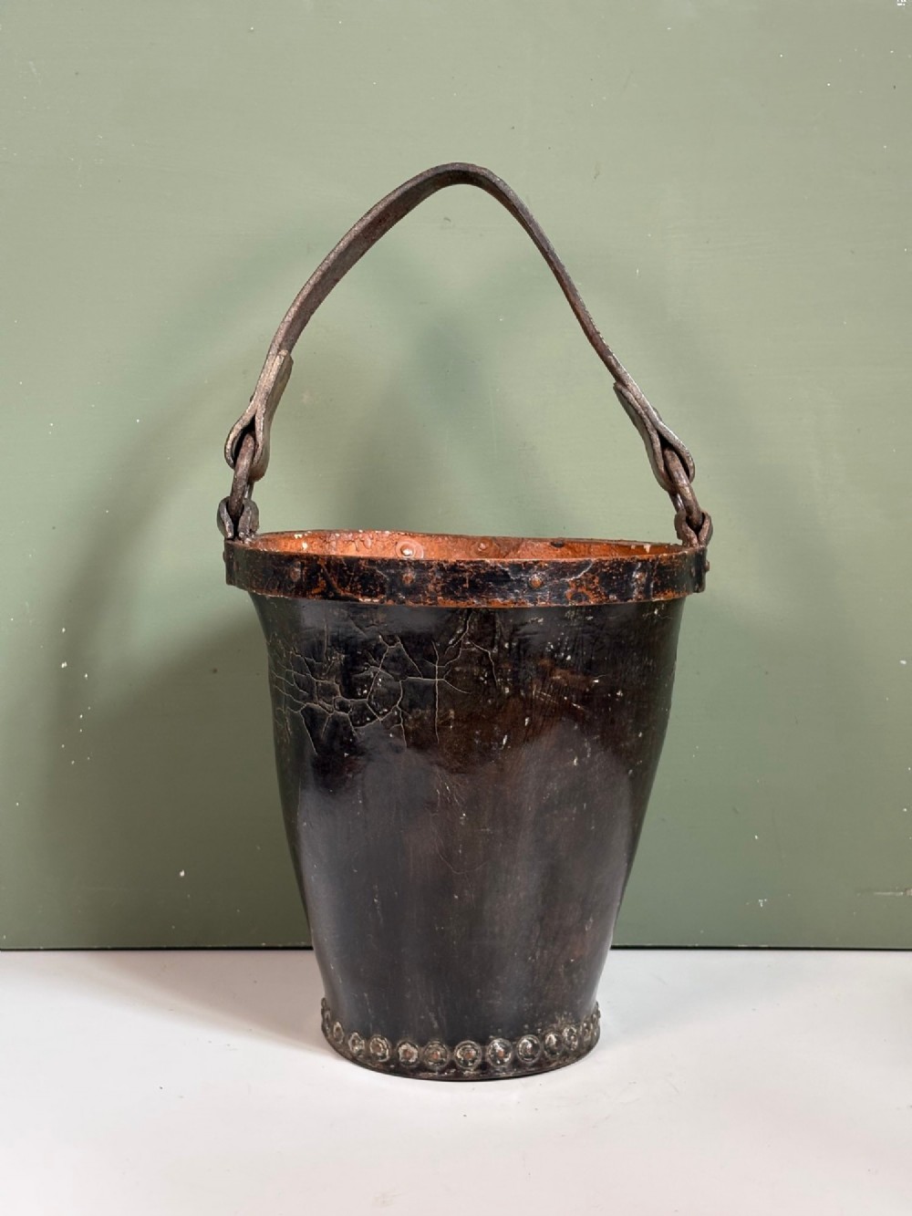 A 19th-century dark brown boiled leather bucket featuring a vertical row of copper rivets down the seam and a metal-reinforced leather strap handle. View II