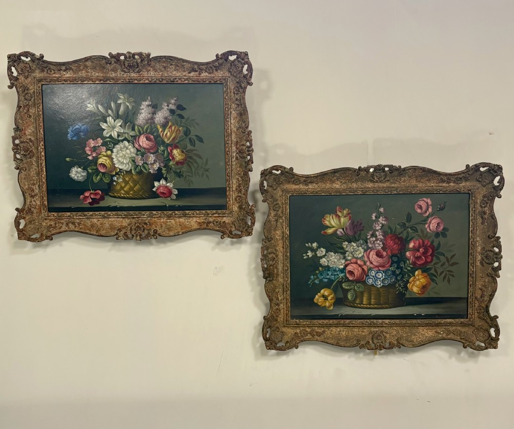 A pair of 19th-century oil paintings displaying botanical floral arrangements in woven baskets within ornate swept gilt frames.