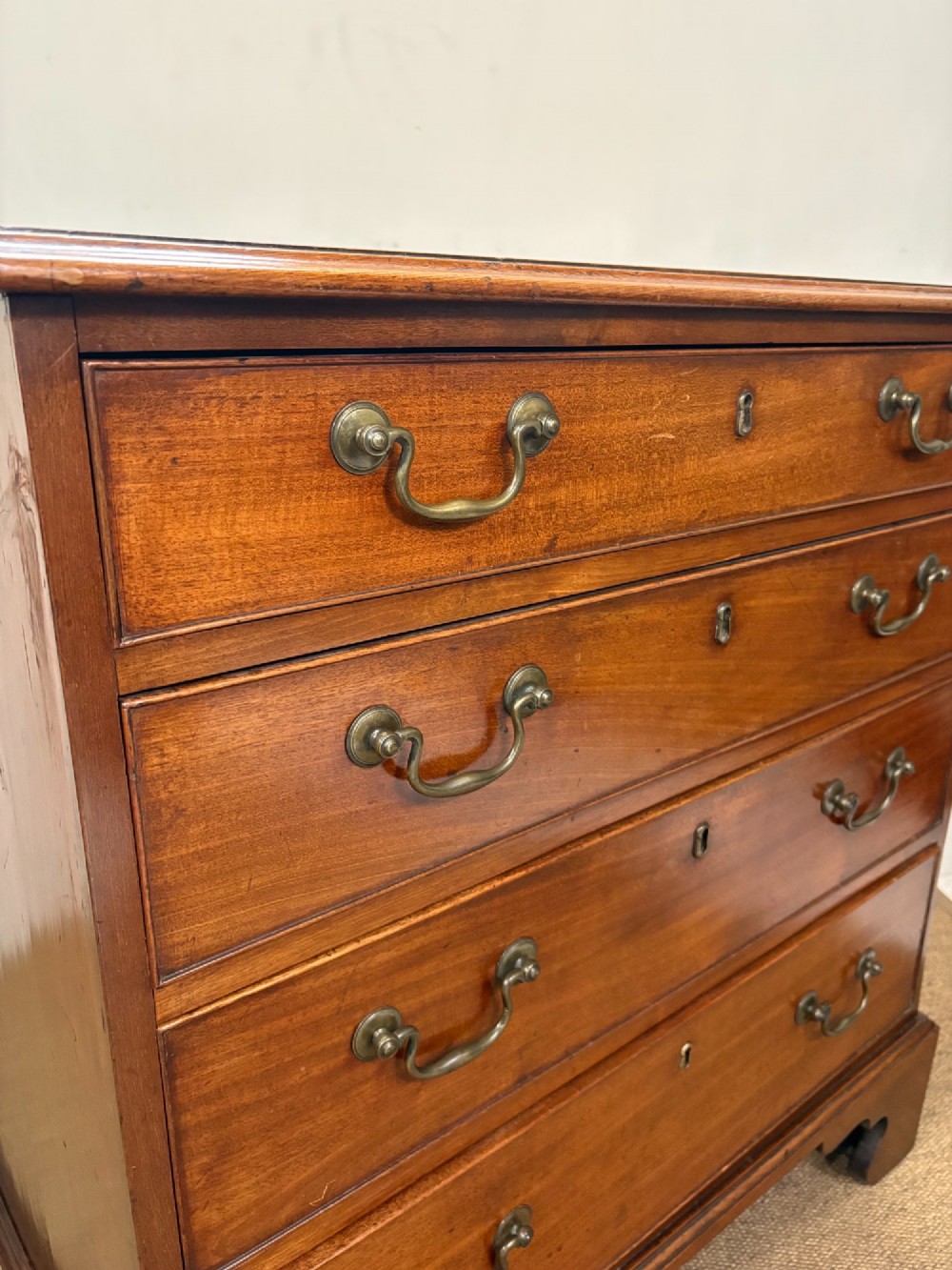 A George III mahogany chest of four graduated drawers with brass swan-neck handles and bracket feet. View IV