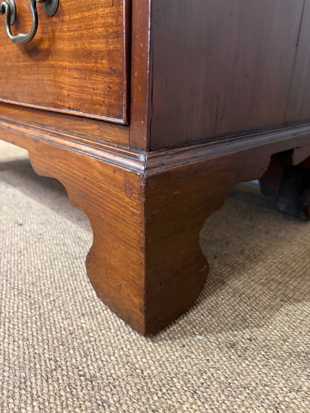 A George III mahogany chest of four graduated drawers with brass swan-neck handles and bracket feet. View V