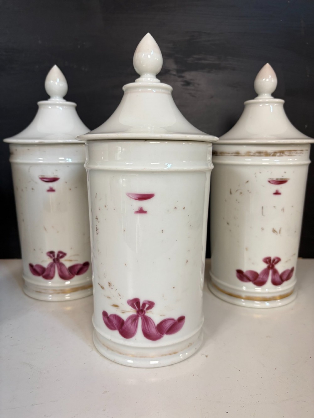 Set of five matching off-white 19th-century porcelain apothecary jars featuring pointed finial lids and hand-painted magenta bow motifs. View III