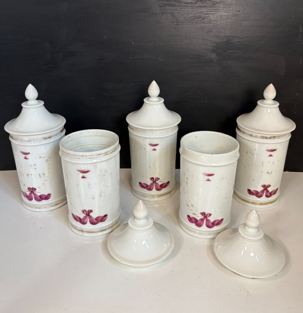 Set of five matching off-white 19th-century porcelain apothecary jars featuring pointed finial lids and hand-painted magenta bow motifs. View IV