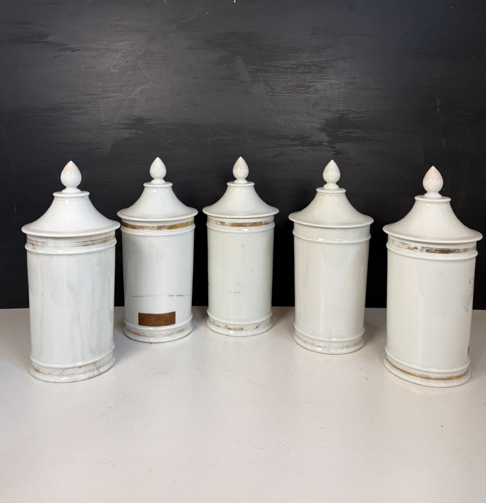 Set of five matching off-white 19th-century porcelain apothecary jars featuring pointed finial lids and hand-painted magenta bow motifs. View VI
