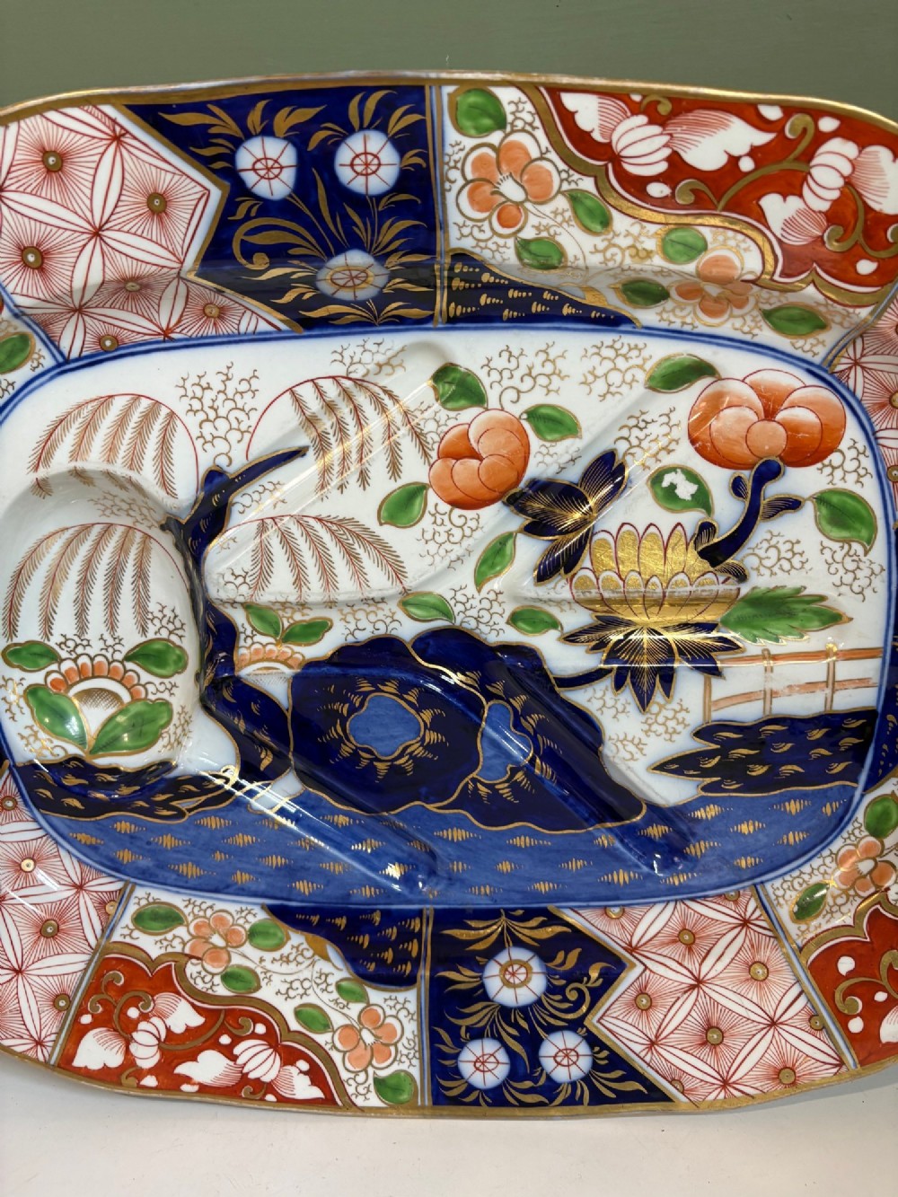 A large oval 19th-century Coalport porcelain meat platter featuring an Imari pattern with cobalt blue, iron red, and gold leaf detailing around a moulded tree-and-well channel. View II