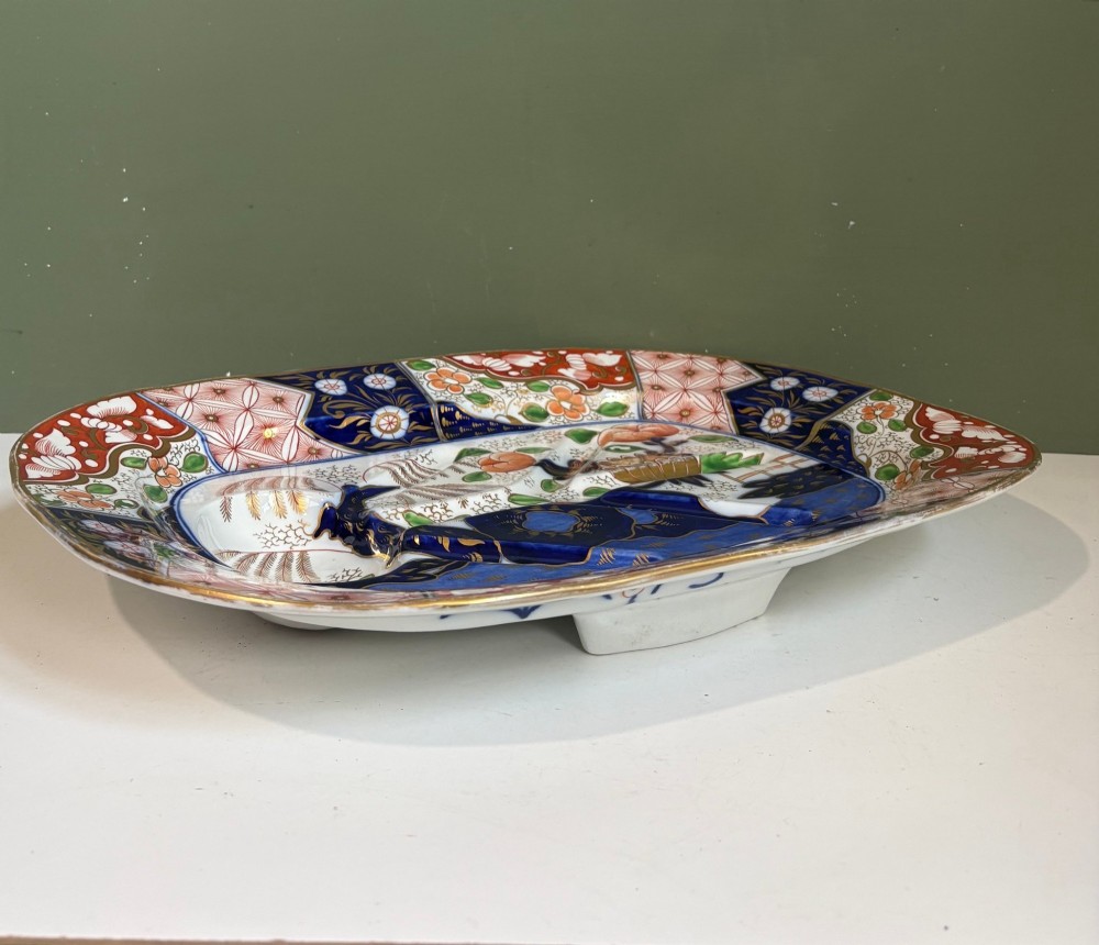 A large oval 19th-century Coalport porcelain meat platter featuring an Imari pattern with cobalt blue, iron red, and gold leaf detailing around a moulded tree-and-well channel. View VI