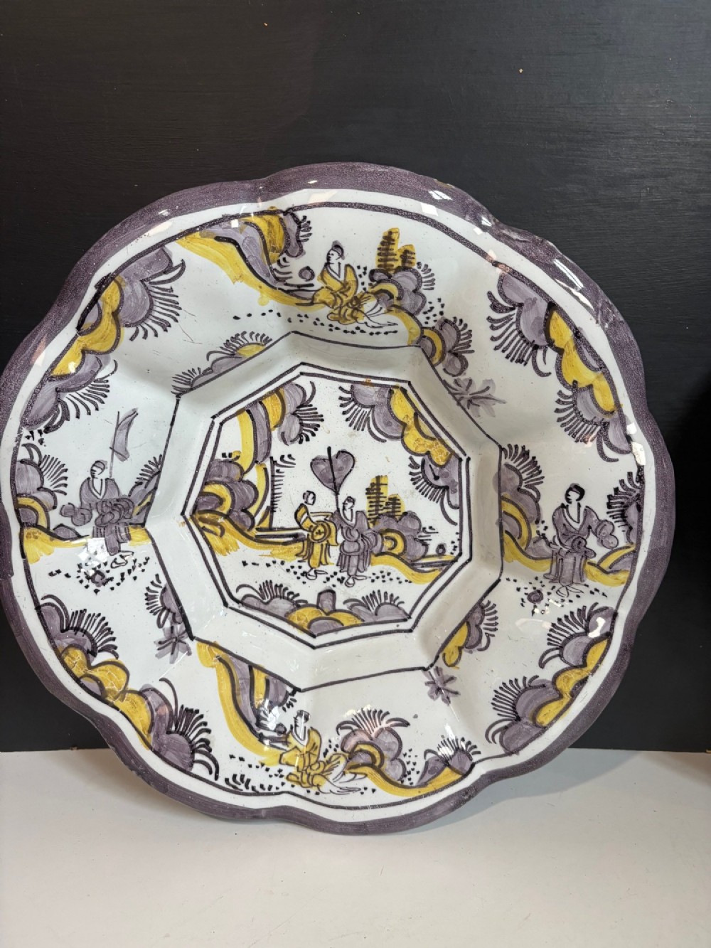 A pair of circular 18th-century tin-glazed earthenware dishes featuring hand-painted manganese purple and yellow chinoiserie figures surrounded by scalloped edges. View III