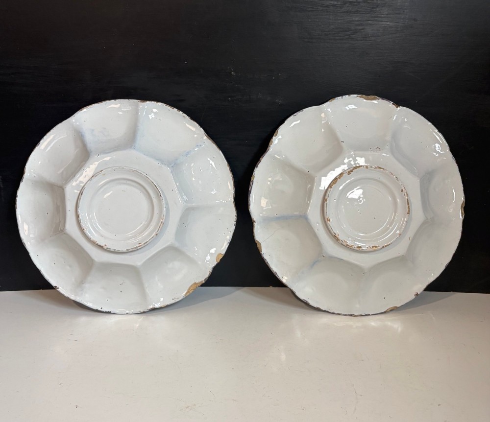 A pair of circular 18th-century tin-glazed earthenware dishes featuring hand-painted manganese purple and yellow chinoiserie figures surrounded by scalloped edges. View V