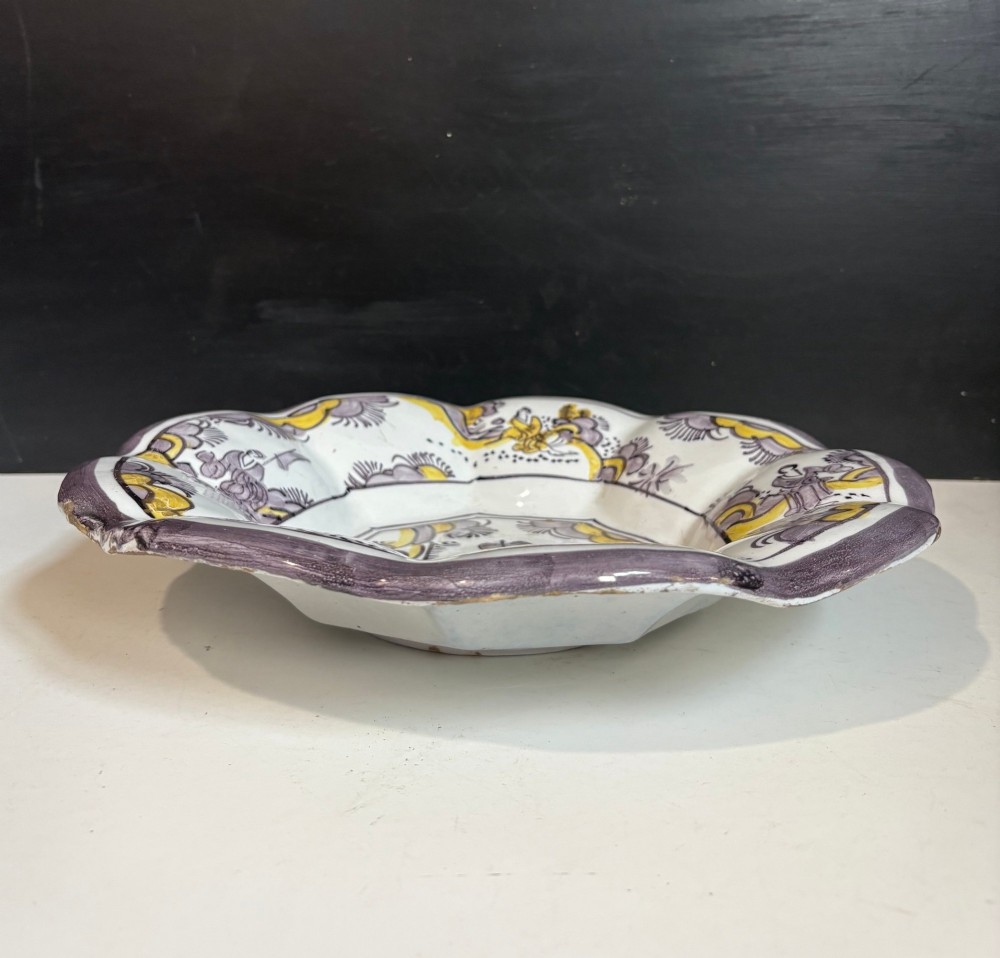 A pair of circular 18th-century tin-glazed earthenware dishes featuring hand-painted manganese purple and yellow chinoiserie figures surrounded by scalloped edges. View VII