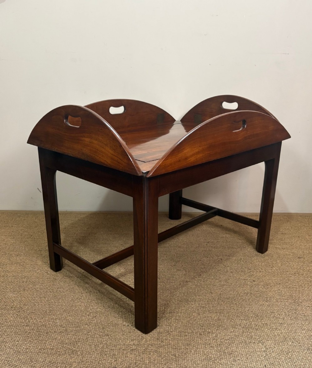 A Georgian mahogany butlers tray with hinged drop sides and cutout handles, resting on a matching wooden table base. View II