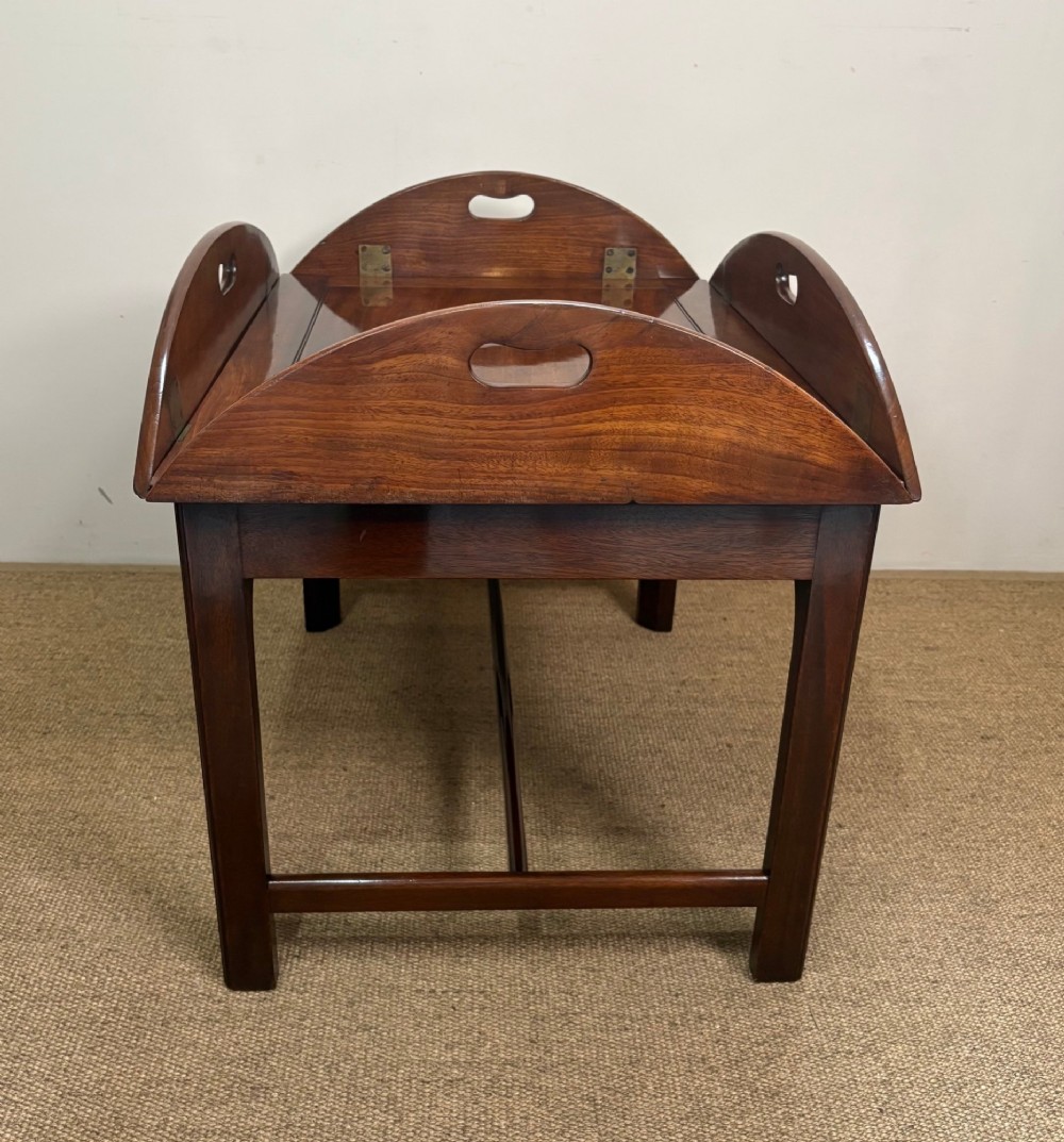 A Georgian mahogany butlers tray with hinged drop sides and cutout handles, resting on a matching wooden table base. View IV