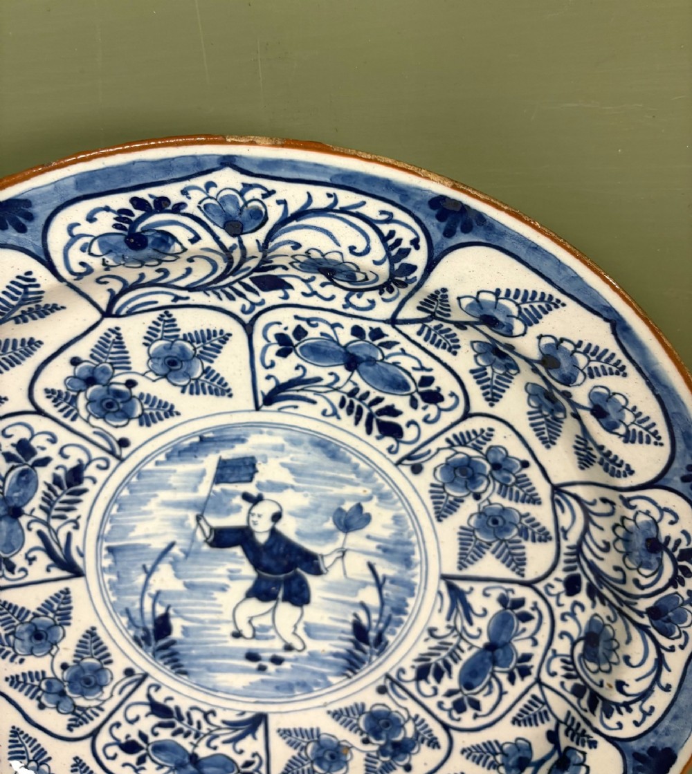 A circular 18th-century tin-glazed earthenware dish decorated in cobalt blue and white with a central Chinoiserie figure surrounded by floral border panels. View II