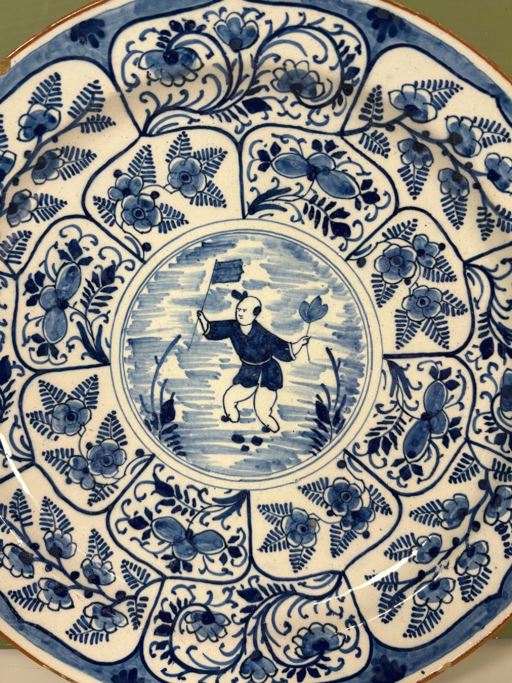 A circular 18th-century tin-glazed earthenware dish decorated in cobalt blue and white with a central Chinoiserie figure surrounded by floral border panels. View III