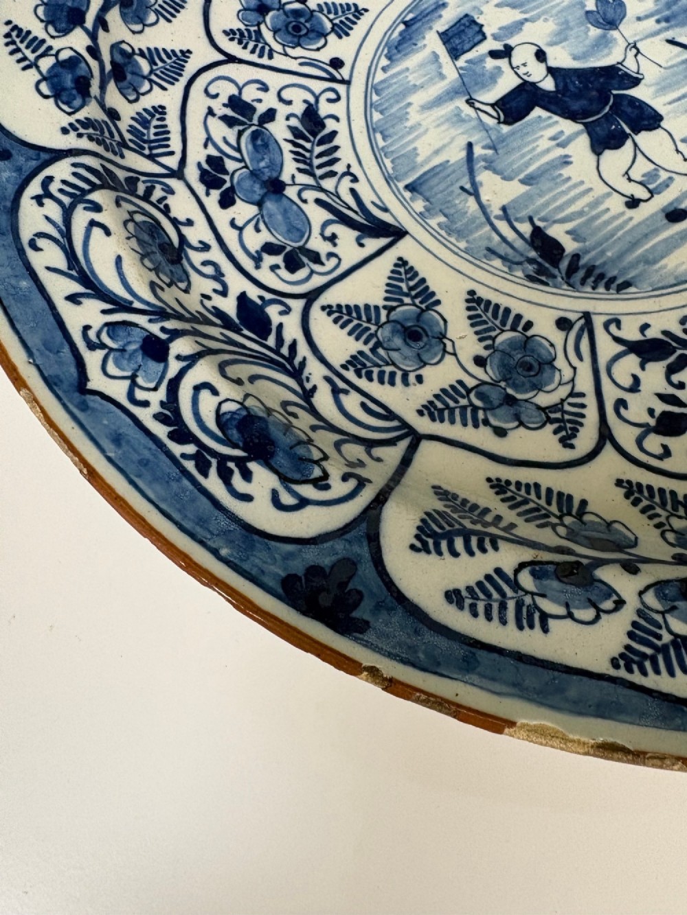 A circular 18th-century tin-glazed earthenware dish decorated in cobalt blue and white with a central Chinoiserie figure surrounded by floral border panels. View VI