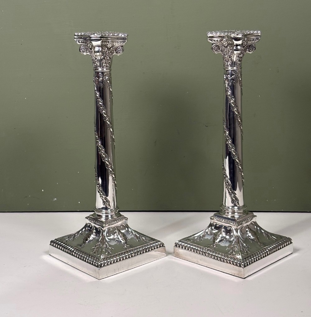A pair of 19th-century silver-plated candlesticks featuring Corinthian capitals, spiral garland columns, and square stepped bases with classical urn reliefs. View II