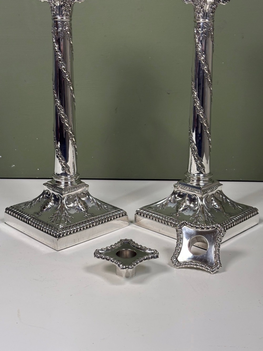 A pair of 19th-century silver-plated candlesticks featuring Corinthian capitals, spiral garland columns, and square stepped bases with classical urn reliefs. View III