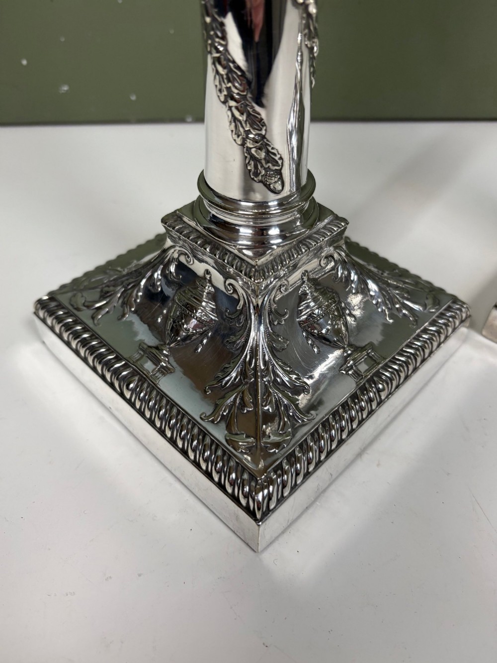 A pair of 19th-century silver-plated candlesticks featuring Corinthian capitals, spiral garland columns, and square stepped bases with classical urn reliefs. View IV