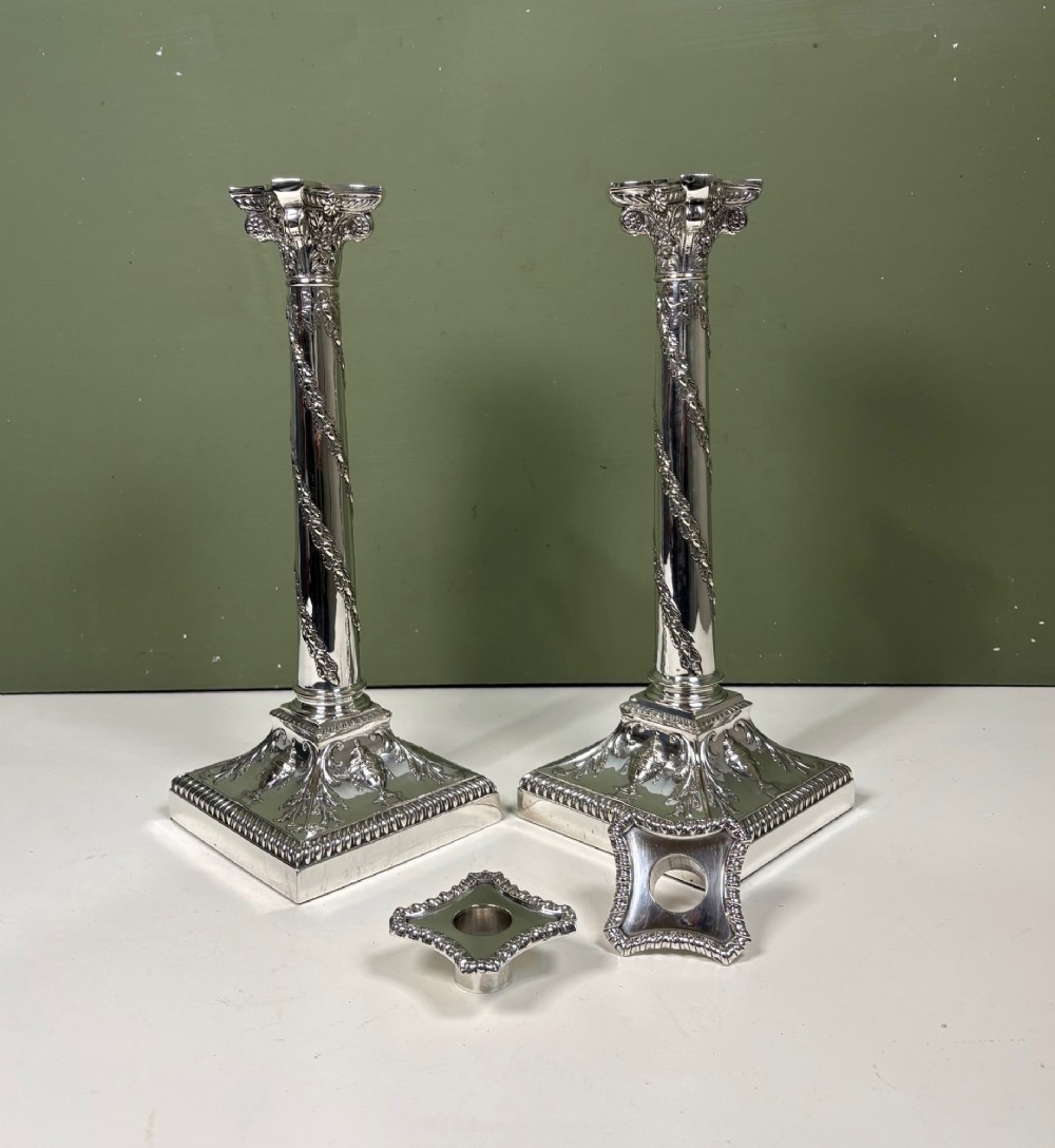 A pair of 19th-century silver-plated candlesticks featuring Corinthian capitals, spiral garland columns, and square stepped bases with classical urn reliefs. View VII
