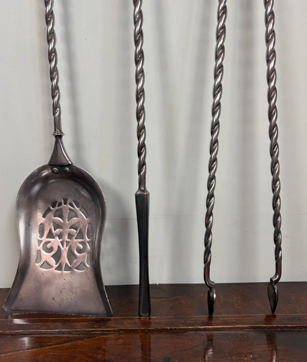 A set of three 19th-century polished steel fire tools including a pierced shovel, poker, and tongs with barley-twist shafts and ornate brass handles. View III