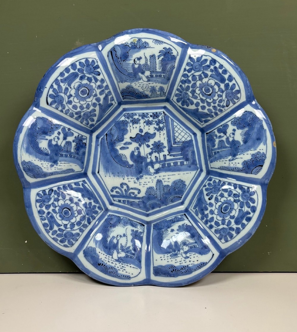 An eighteenth-century lobed tin-glazed earthenware dish featuring cobalt blue hand-painted chinoiserie figures and floral scrollwork within segmented panels.