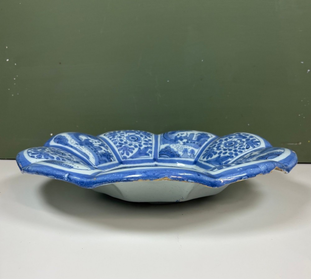 An eighteenth-century lobed tin-glazed earthenware dish featuring cobalt blue hand-painted chinoiserie figures and floral scrollwork within segmented panels. View VI