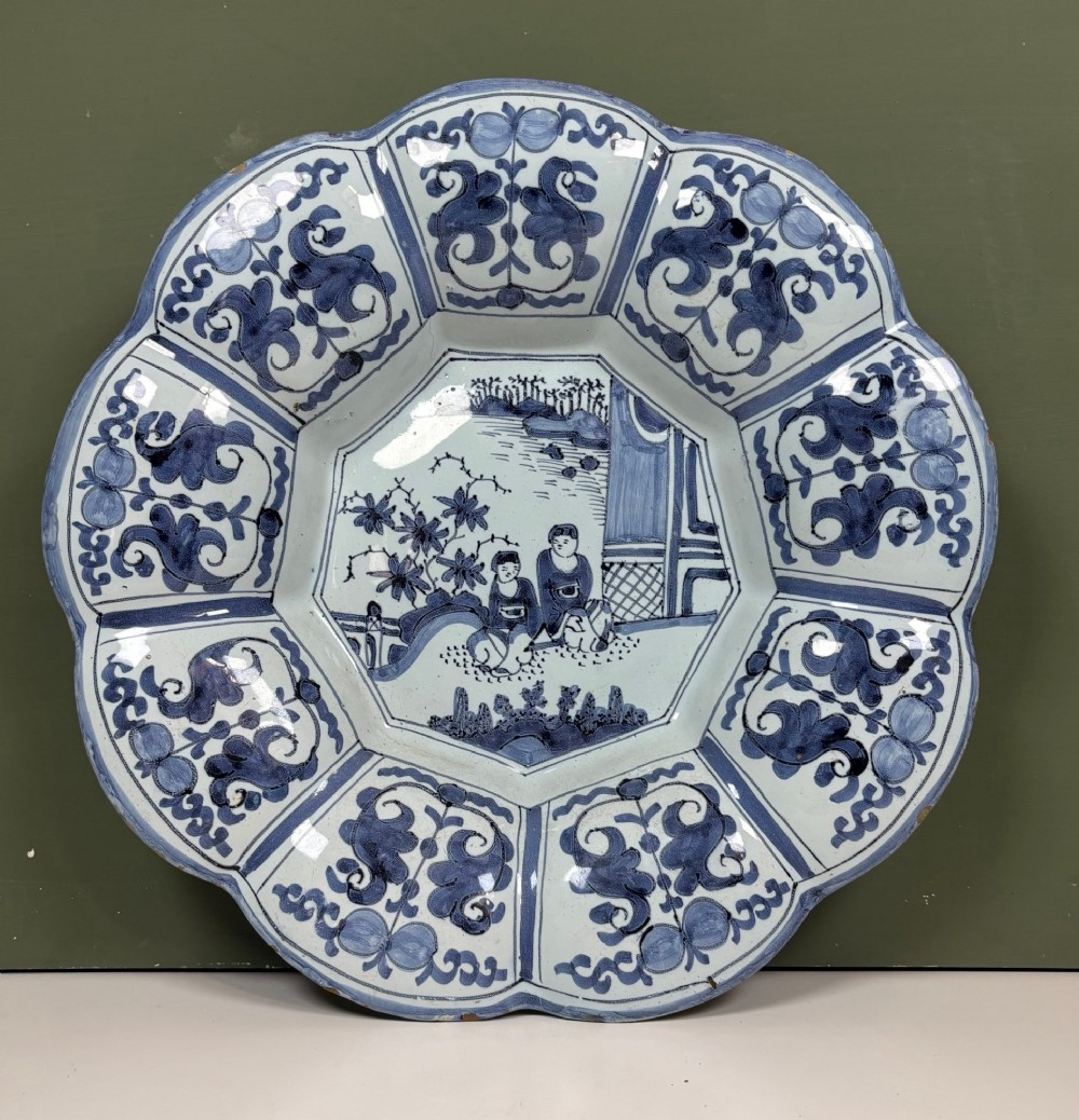 An 18th-century scalloped tin-glazed earthenware dish decorated with hand-painted cobalt blue Chinoiserie figures and floral patterns.