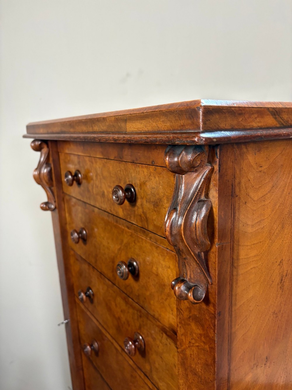 A tall Victorian walnut Wellington chest featuring six drawer fronts, carved corbels, and an open drop-front secretaire revealing internal pigeonholes and small drawers. View V