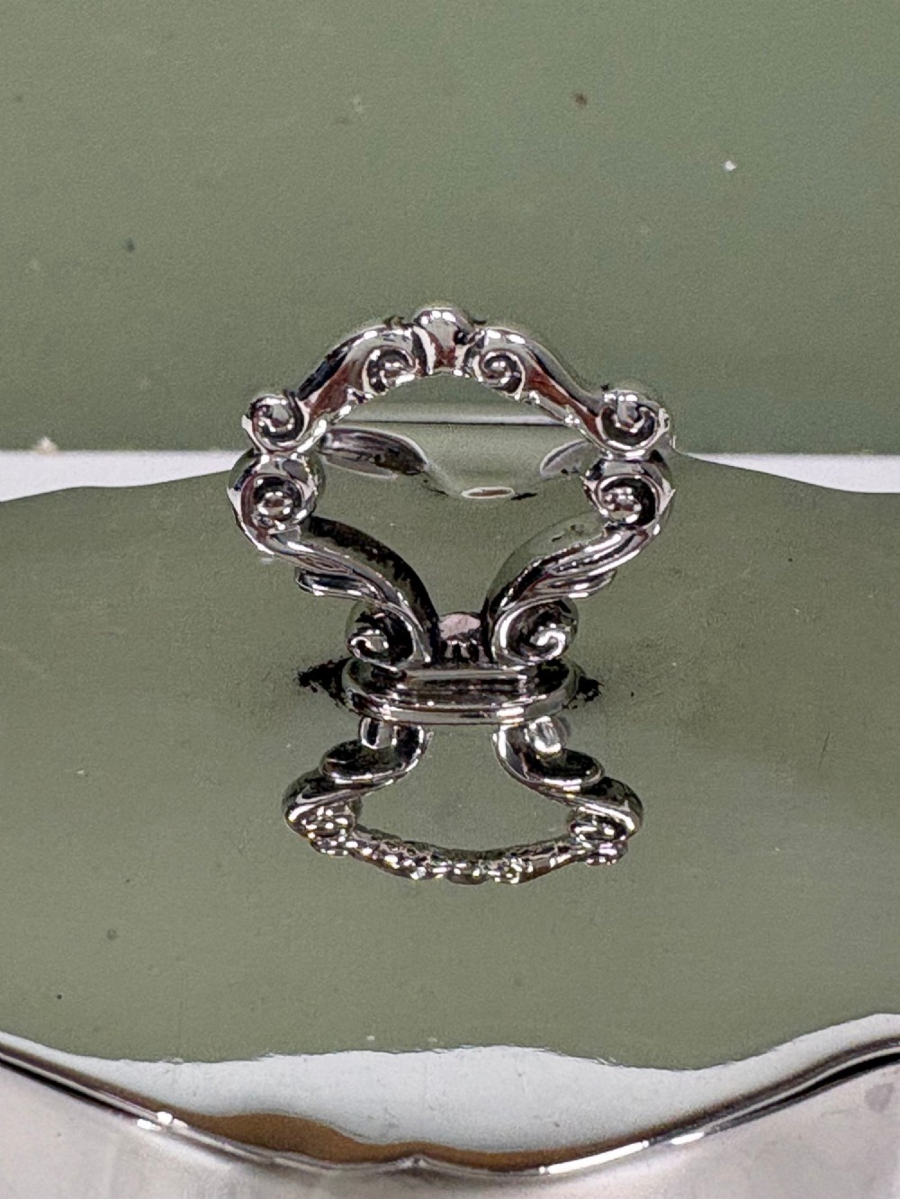 A polished cylindrical solid silver caddy featuring lobed vertical panels, a fitted flush lid, and an ornate scroll finial handle. View V