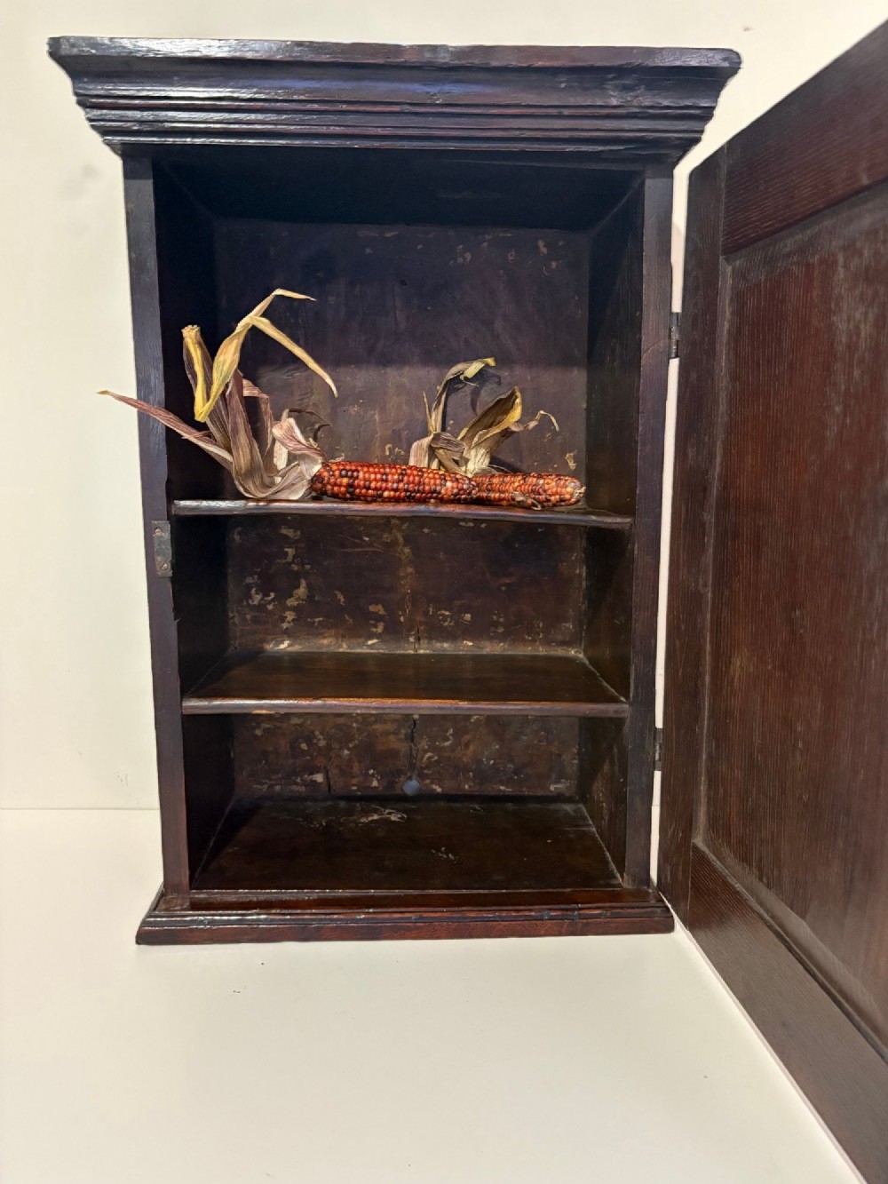 An eighteenth-century dark oak wall cupboard with a single field-panel door, brass keyhole escutcheon, and moulded top cornice. View II