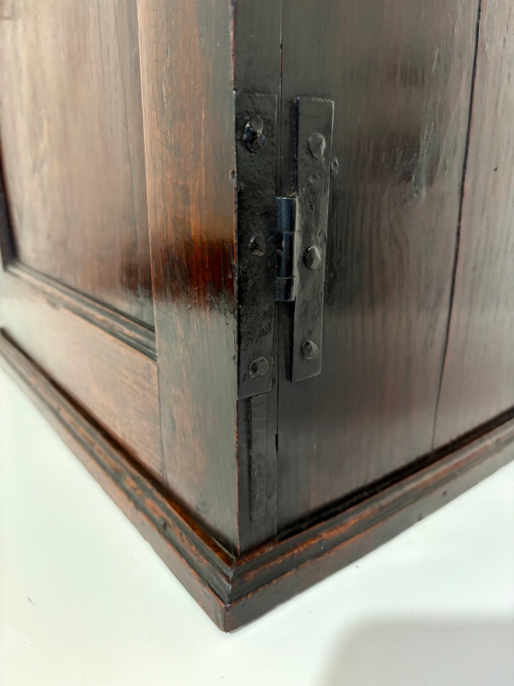 An eighteenth-century dark oak wall cupboard with a single field-panel door, brass keyhole escutcheon, and moulded top cornice. View VI