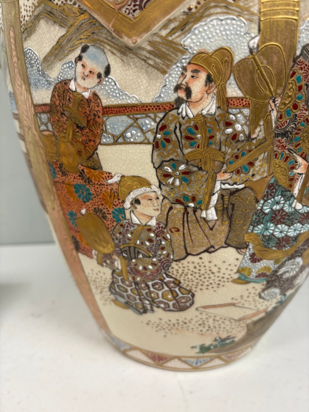 A large Japanese Satsuma earthenware lidded vase featuring intricate gilding, figural panels, a scalloped collar, and a gilded foo dog finial. View VI