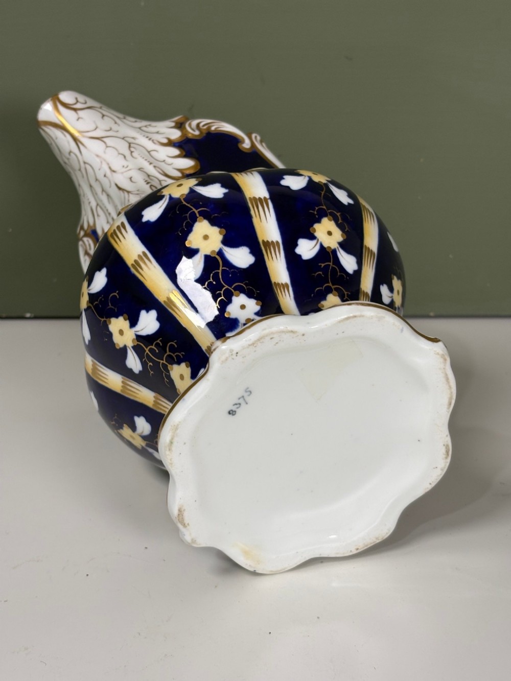 A nineteenth-century cobalt blue porcelain jug with gold gilding, white floral pattern, an ornate scroll handle, and a scalloped spout. View VI