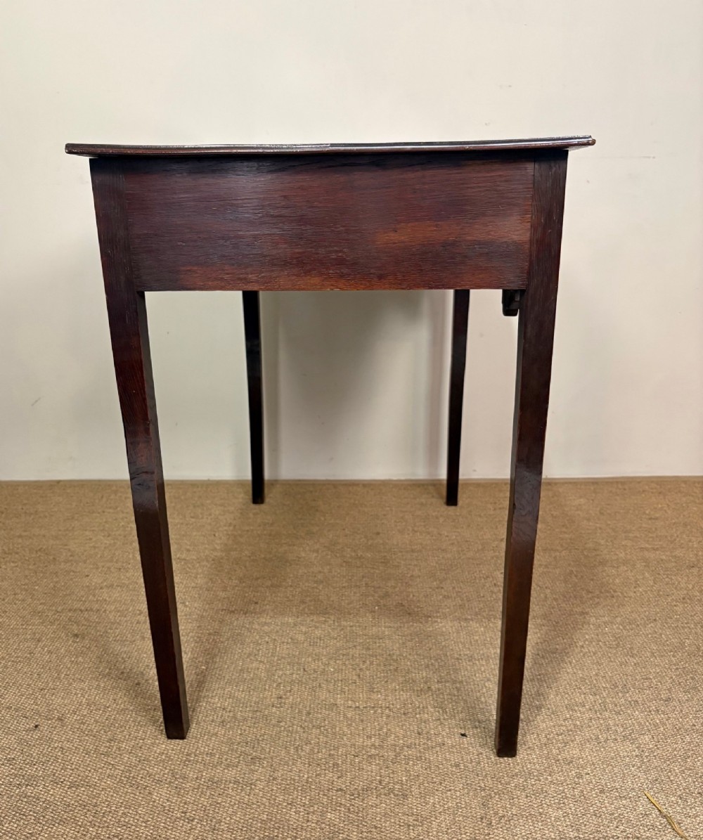 An 18th-century dark oak lowboy side table featuring three drawers with circular brass drop handles and a shaped scalloped apron supported by four straight legs. View VI