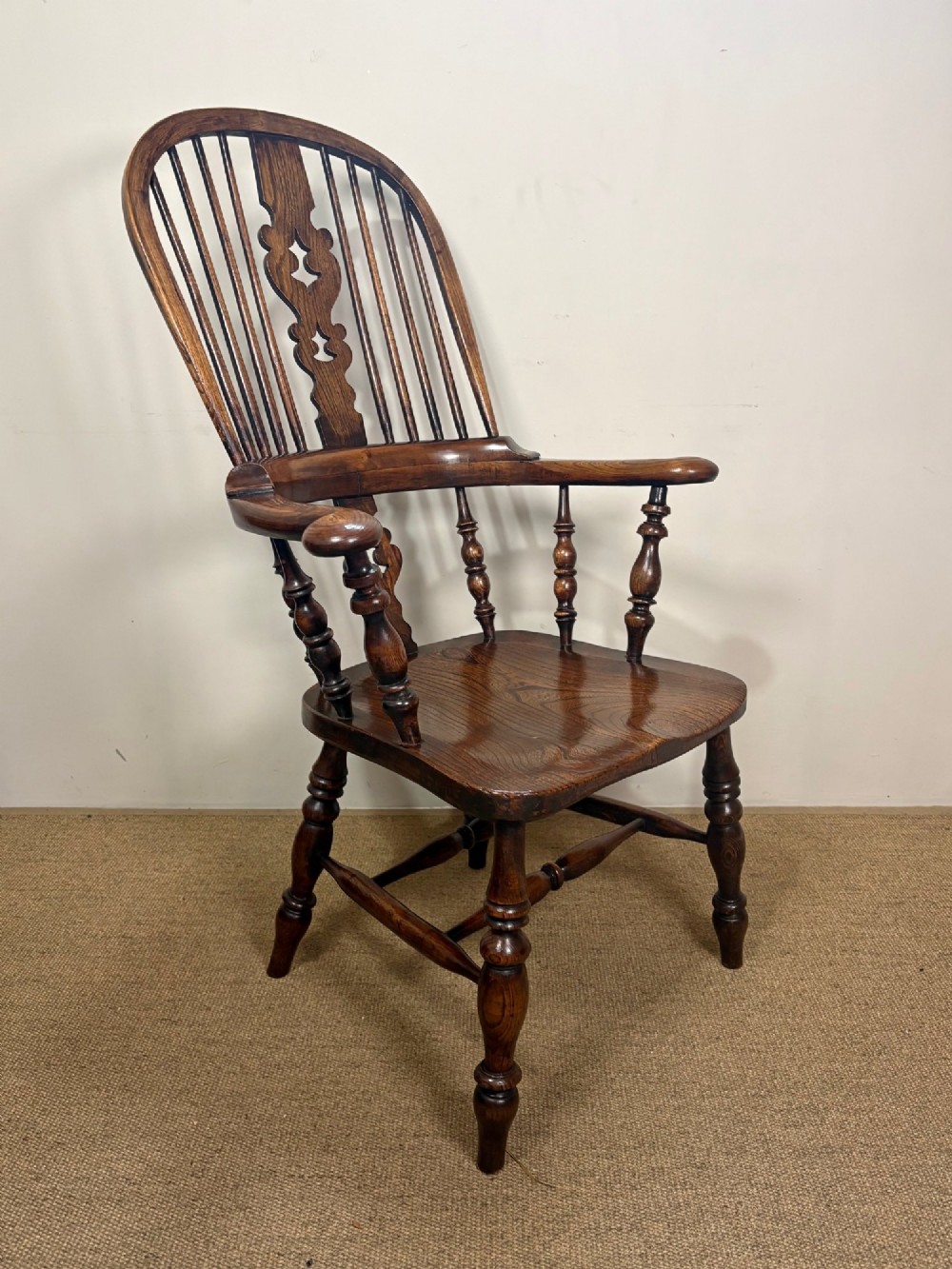 A 19th-century dark oak and elm Windsor armchair featuring a hoop back, central pierced splat, turned arm supports, and turned legs joined by stretchers.