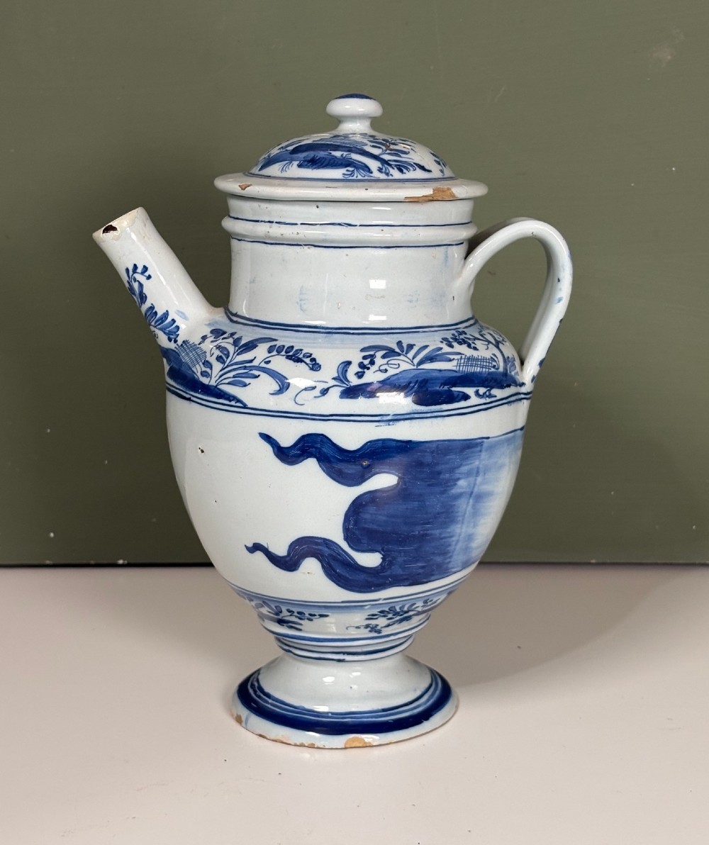 An 18th-century blue and white tin-glazed Delftware spouted apothecary jar featuring a fitted lid, side handle, and painted foliate decoration.