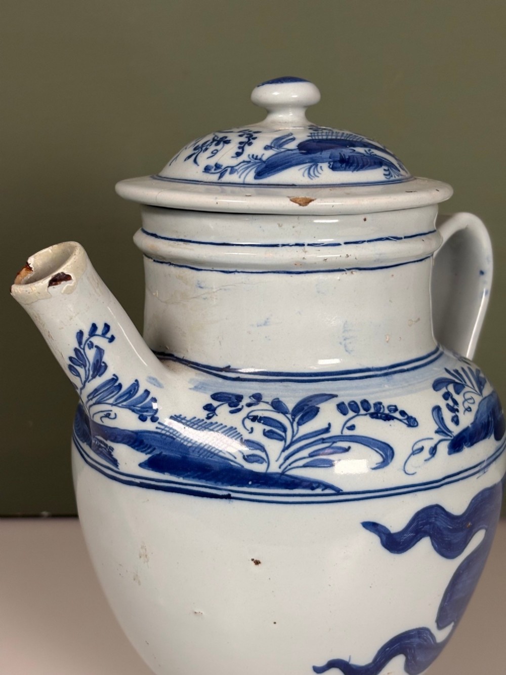 An 18th-century blue and white tin-glazed Delftware spouted apothecary jar featuring a fitted lid, side handle, and painted foliate decoration. View IV