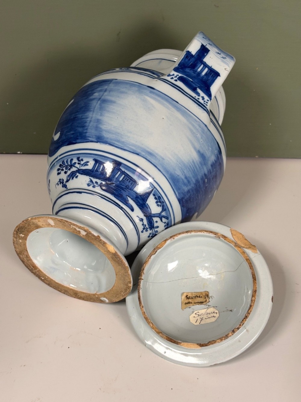 An 18th-century blue and white tin-glazed Delftware spouted apothecary jar featuring a fitted lid, side handle, and painted foliate decoration. View V