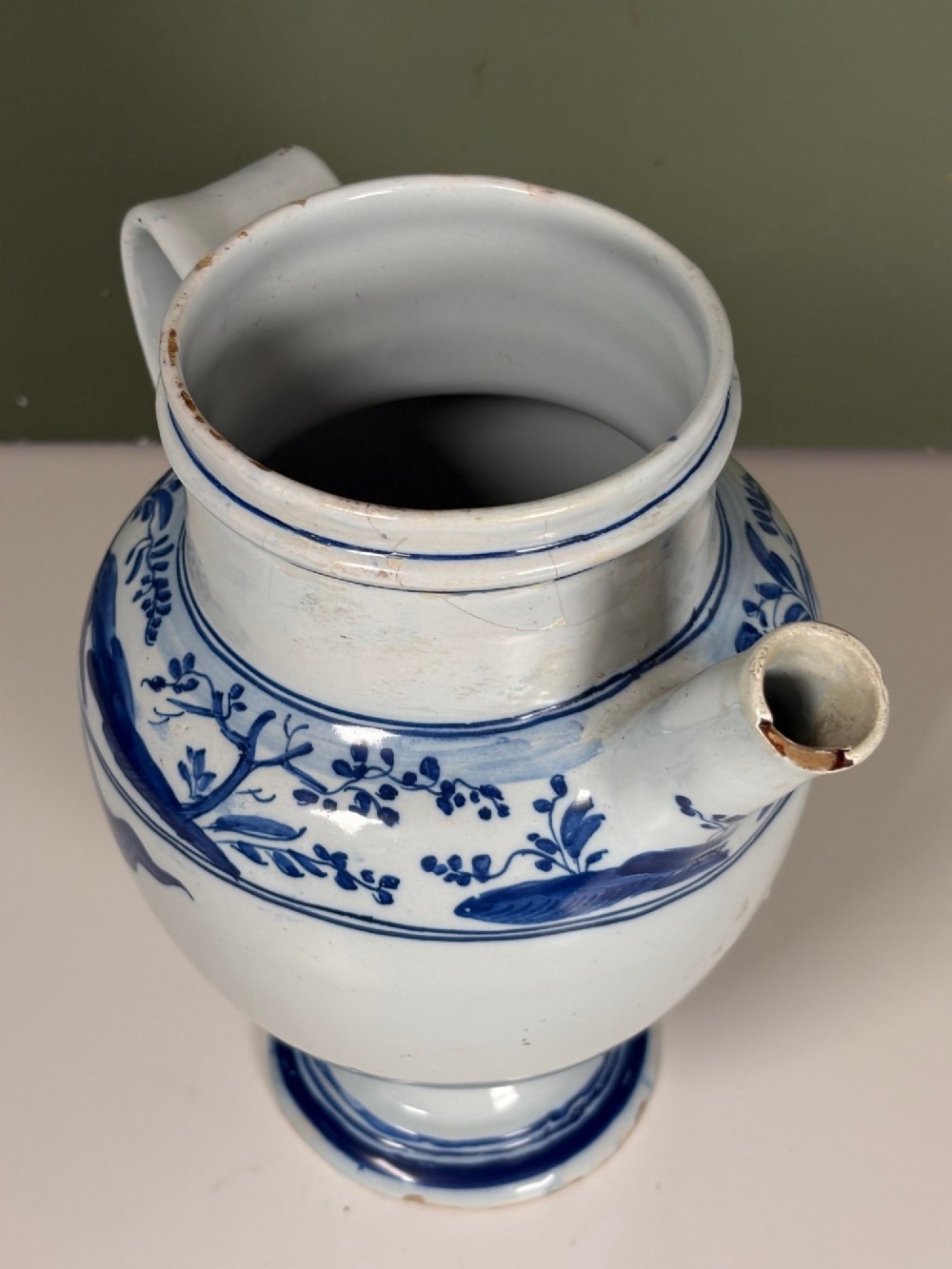 An 18th-century blue and white tin-glazed Delftware spouted apothecary jar featuring a fitted lid, side handle, and painted foliate decoration. View VII
