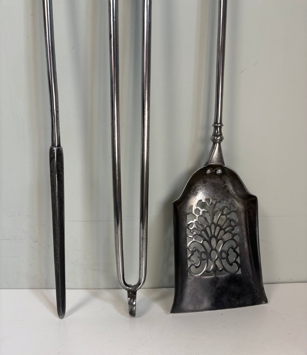 A set of three 18th-century steel fire tools, including a poker, tongs, and a pierced shovel, topped with decorative brass finials. View II