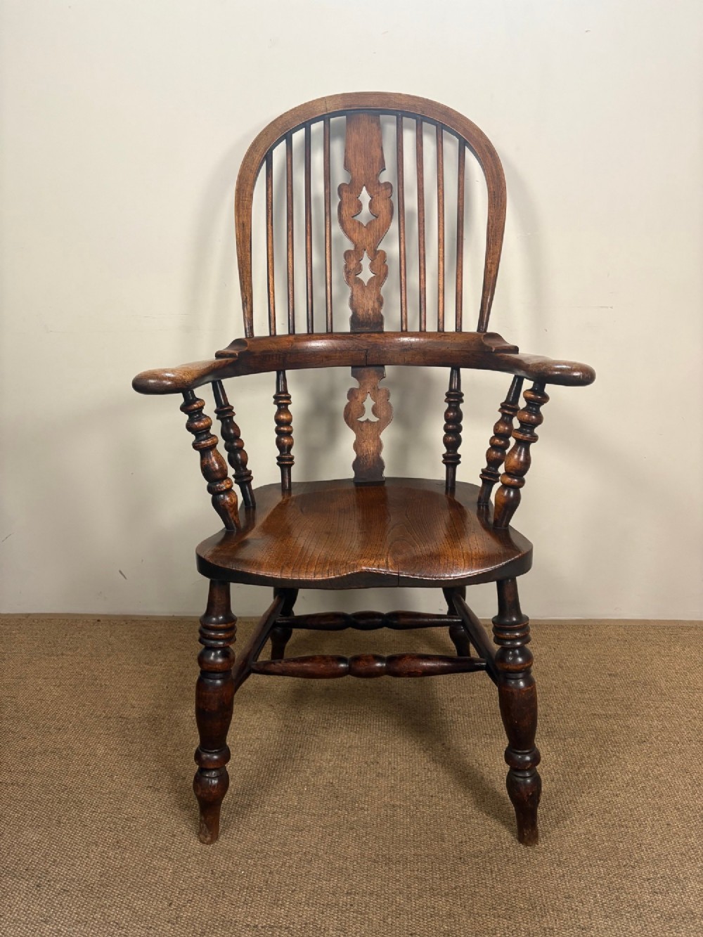 A 19th-century oak and elm Windsor armchair featuring a high hoop back, turned spindles, a pierced central splat, turned legs, and a solid saddle seat.