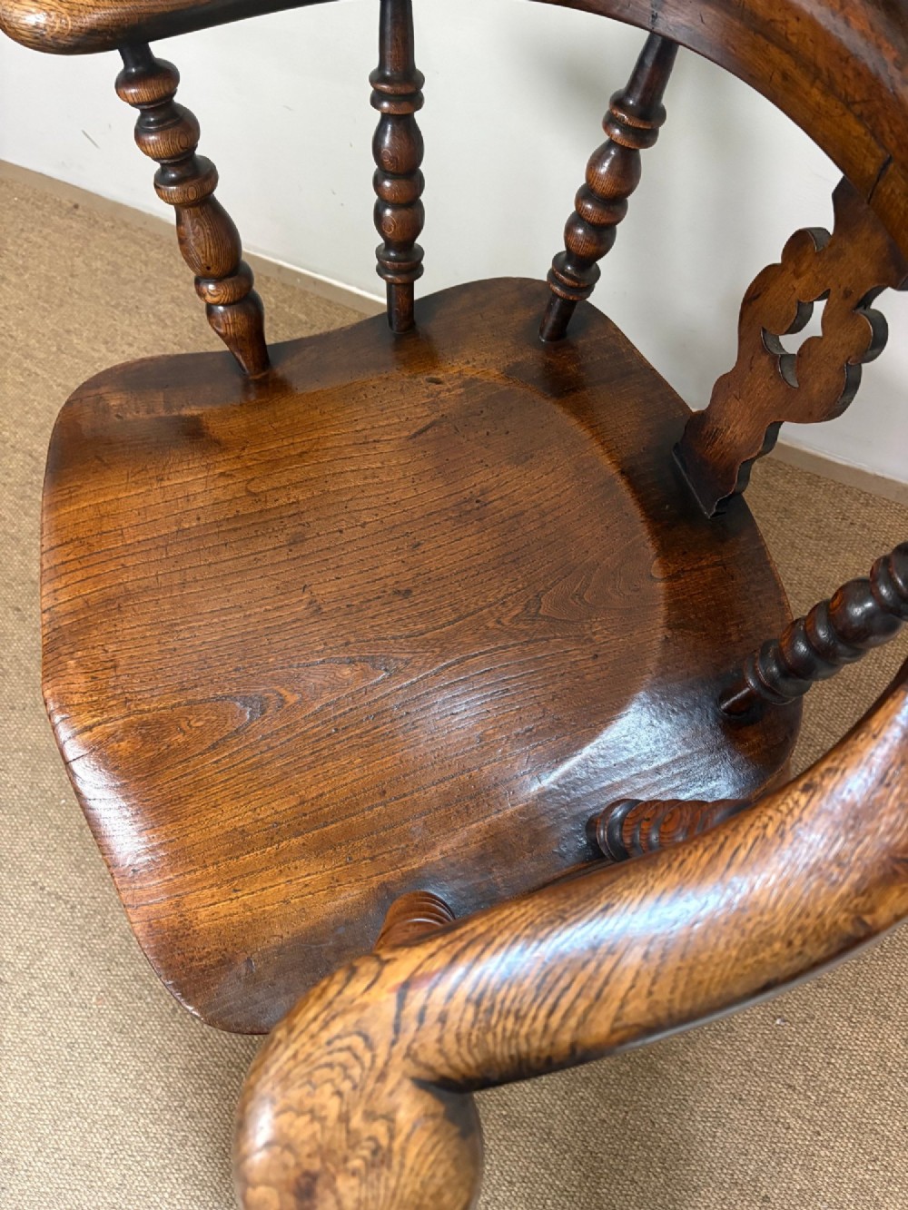 A 19th-century oak and elm Windsor armchair featuring a high hoop back, turned spindles, a pierced central splat, turned legs, and a solid saddle seat. View V