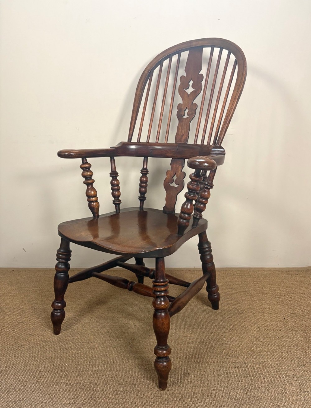 A nineteenth-century elm and beech Windsor armchair featuring a high hoop back, pierced central splat, turned spindles, curved armrests, and turned legs linked by an H-stretcher.